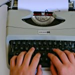 Close-up of hands typing on a classic Underwood typewriter with paper.